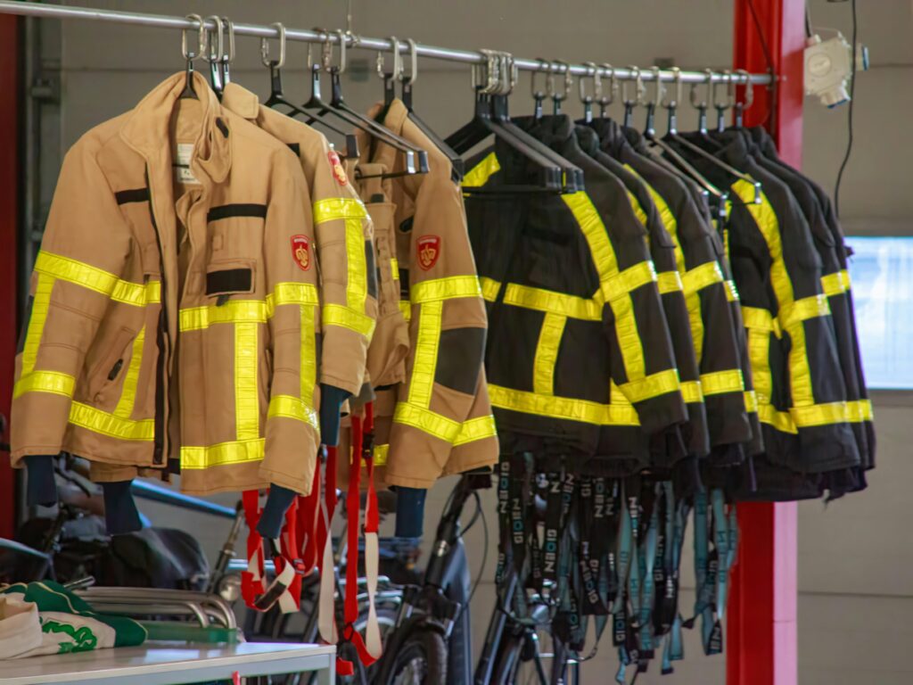 Firefighter uniforms with reflective strips hanging in a garage setting.